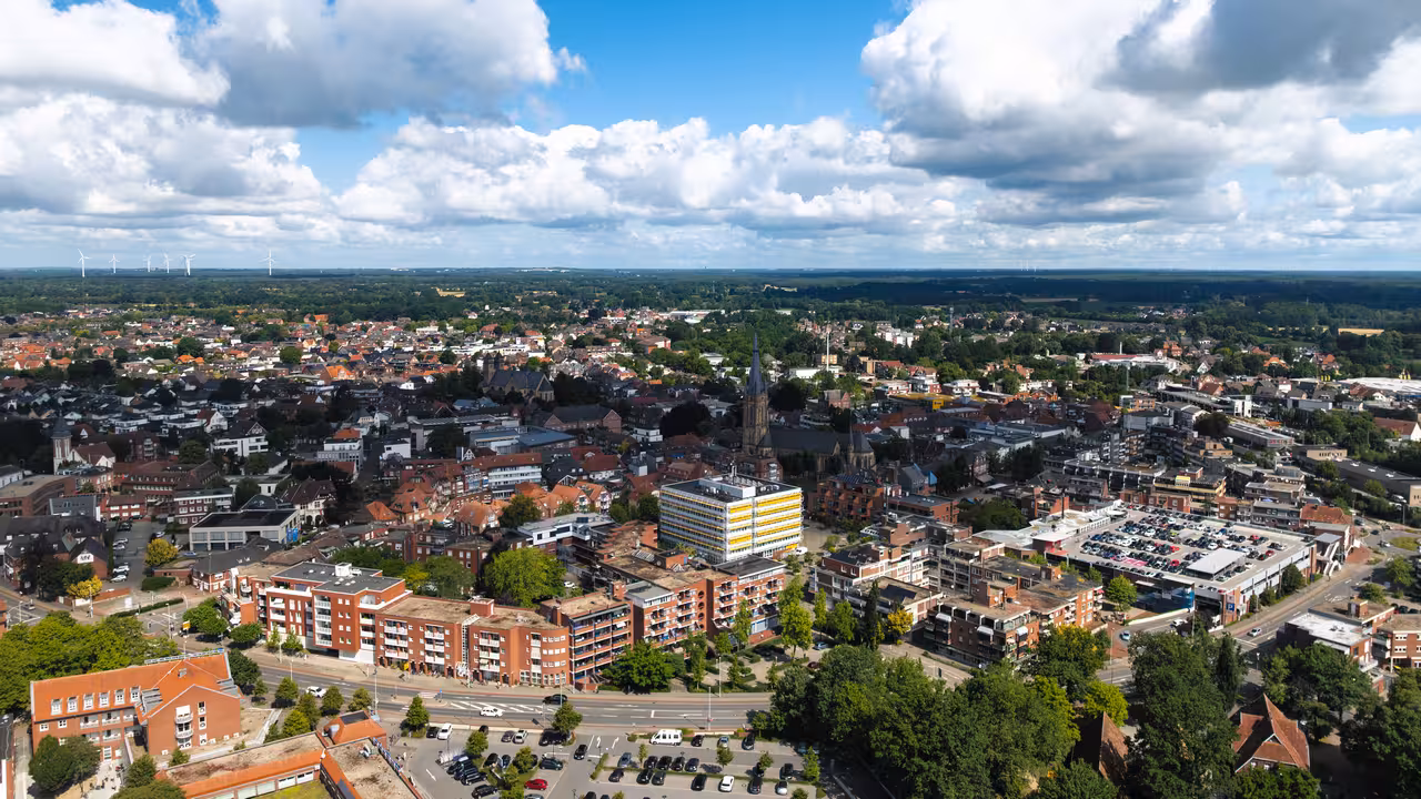 drohnenaufnahme einer hauptstraße im umliegenden stadtgebiet mit wohnbebauung, einem parkhaus und einer kirche in emsdetten