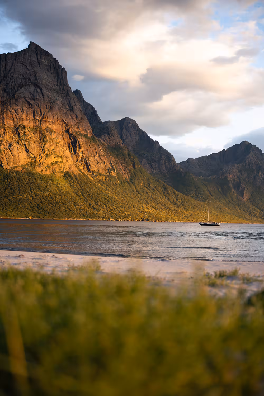 teleaufnahme eines ankernden segelboots in einer meeresbucht mit sandstrand und markanter bergkette im hintergrund in norwegen bei sonnenuntergang