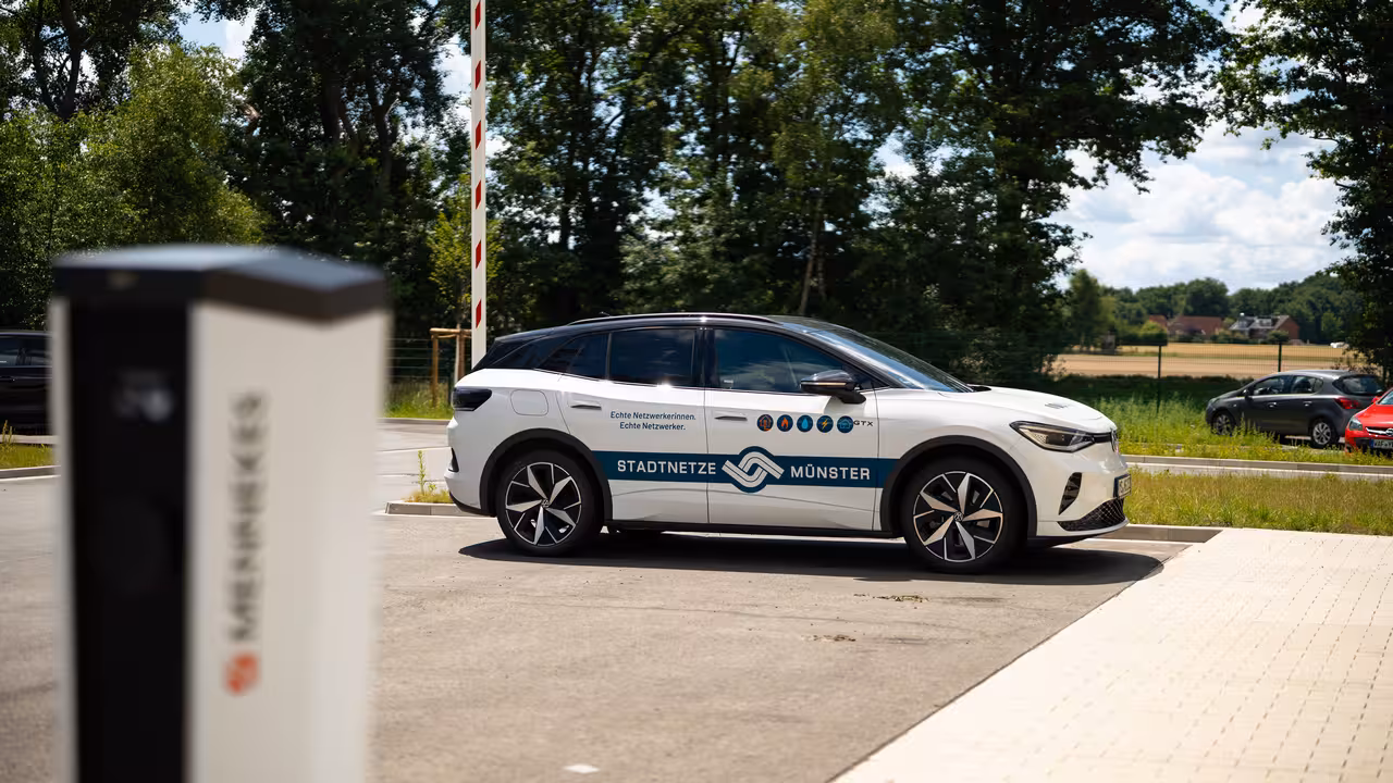 teleaufnahme eines volkswagen elektroautos (id4) mit einer e-ladesäule im vordergrund auf dem gelände eines wasserwerks in münster für immobilienmarketing