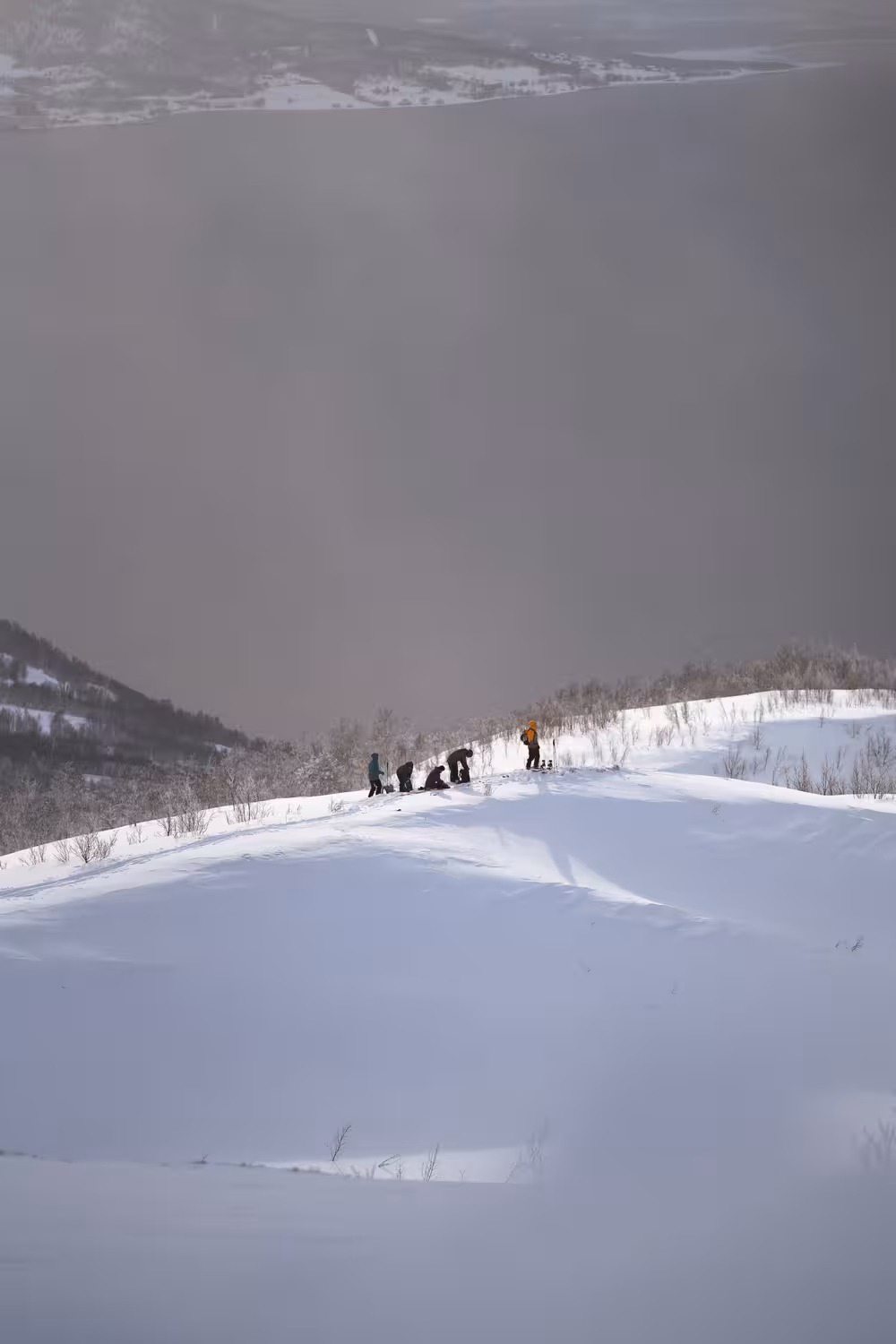 teleaufnahme einer verschneiten berglandschaft mit fünf ski- und snowboardfahrern auf einem hang vor der abfahrt bei schlechten sichtbedingungen bei tromso für das marketing des reiseveranstalters