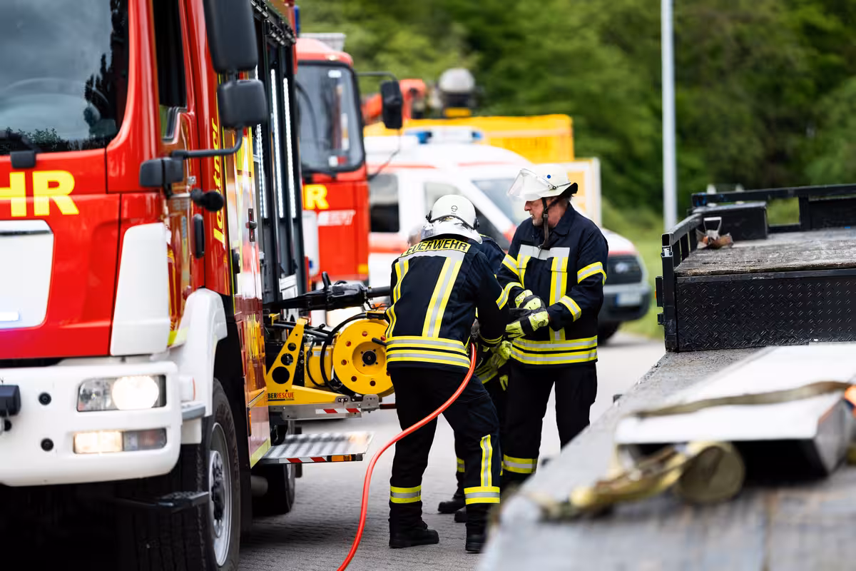 teleaufnahme von drei feuerwehrmännern mit wasserschlauch an einem einsatzfahrzeug während einer rettungsübung für social media